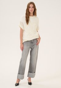 White knitted sweater with textured design, paired with relaxed grey jeans featuring frayed cuffs and black pointed-toe heels.