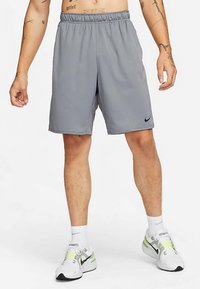 Sive športne kratke hlače iz lahkega materiala z elastičnim pasom in majhnim črnim logotipom Nike na levi nogi.