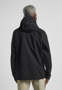 Schwarze wasserdichte Jacke mit Kapuze, die eine glatte Textur und eine lockere Passform aufweist. Sichtbare Nähte und keine auffälligen Logos oder Muster.