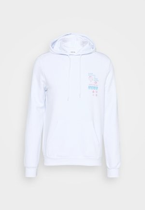 Pantalons cargo beiges avec plusieurs poches, associés à un hoodie blanc avec un design graphique, et des baskets de sport blanches avec des accents noirs.