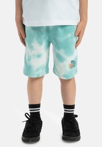 Tyrkysové šortky s farbením tie-dye a jemnou textúrou; s vyšitým logom palmovej tree; spárované s čiernymi topánkami a pruhovanými ponožkami.
