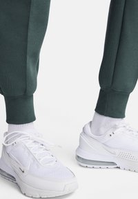 Gröna bomulls-sweatpants med elastiska muddar, kombinerade med vita Nike-sneakers i mesh med synlig luftdämpning och reflekterande detaljer.