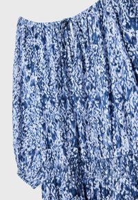 Blouse à motifs floraux bleu et blanc, épaules dénudées, avec encolure, manches et taille élastiquées, ornée d'un petit lien à l'avant.