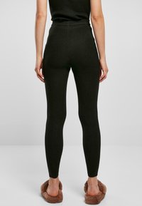 Ribbede, mørkegrønne leggings med høyt liv og tettsittende passform, kombinert med brune, pelsaktige tøfler. Strukturert stoff øker det visuelle interessen.