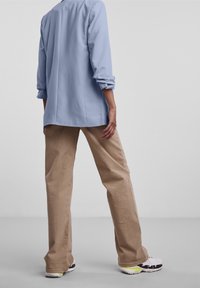 Blazer bleu clair à manches longues, associé à un pantalon beige à jambes larges. La tenue est complétée par des baskets blanches avec des accents noirs et jaune néon.