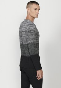 Pulover din tricot gri, cu un model texturat și accente mai închise la baza puloverului, mâneci lungi și guler rotund.