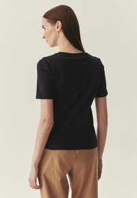 Haut noir moulant à manches courtes en coton doux avec un col rond, porté avec un pantalon beige. Le dos présente un design simple.