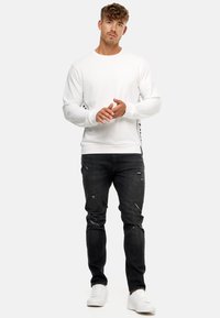 Sudadera blanca con detalles de rayas en los laterales, combinada con jeans negros desgastados y zapatillas blancas. Tela suave, corte casual y diseño de cuello redondo.