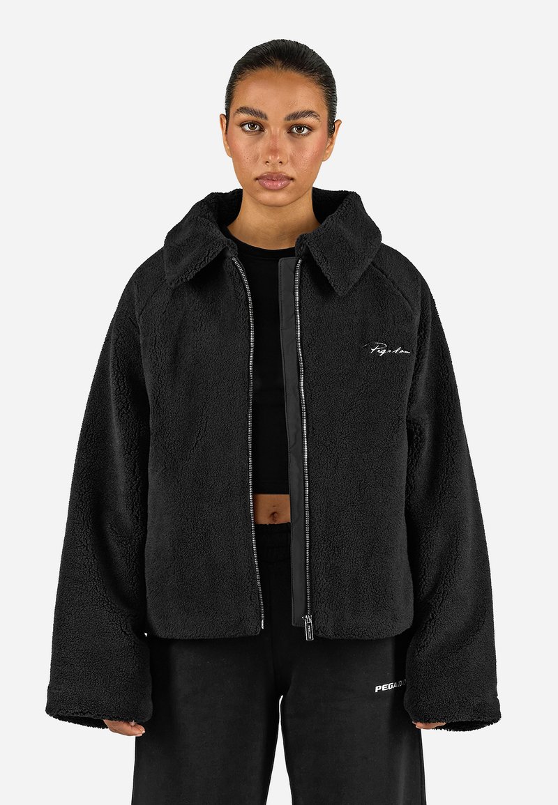 Giacca in pile nera con un taglio ampio, colletto largo, chiusura con zip e dettaglio del logo ricamato sul petto. Tessuto morbido e maniche oversize.