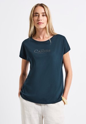 T-shirt à manches courtes bleu marine avec un col rond, arborant un logo "CANNES" imprimé en gris clair. Texture de tissu douce et lisse.