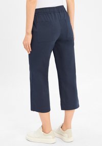 Marineblauwe cropped pantalons met een relaxte pasvorm, elastische tailleband, twee achterzakken en een zachte katoenen textuur. Gecombineerd met witte sneakers.