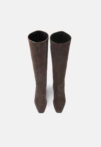 Bottes en daim marron jusqu'au genou avec un bout pointu et une doublure intérieure lisse. Le design présente des coutures minimales et une silhouette épurée.