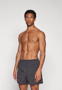 Boxer shorts in dark gray with thin vertical stripes, made from lightweight fabric. Features an elastic waistband and a front button closure.