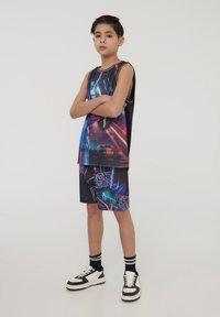 Canotta grafica nera con design di auto neon e accenti colorati, abbinata a pantaloni corti coordinati con loghi. Sneakers bianche e nere.