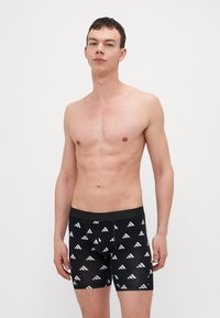 Fekete boxer alsónadrág fehér geometrikus háromszög mintával, puha anyagból, elasztikus derékrésszel és kényelmes, szabott fazonnal.