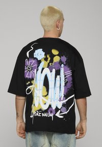 Černé tričko s nápaditým graffiti designem ve výrazných modrých, žlutých a fialových barvách, s výrazným nápisem "WOW!".