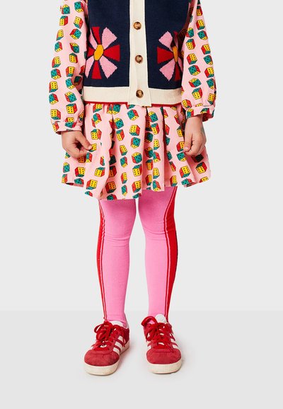 Abito colorato con base rosa e motivi a cubo, sovrapposto a un cardigan navy con motivi floreali. Leggings rosa con strisce rosse e sneakers rosse.
