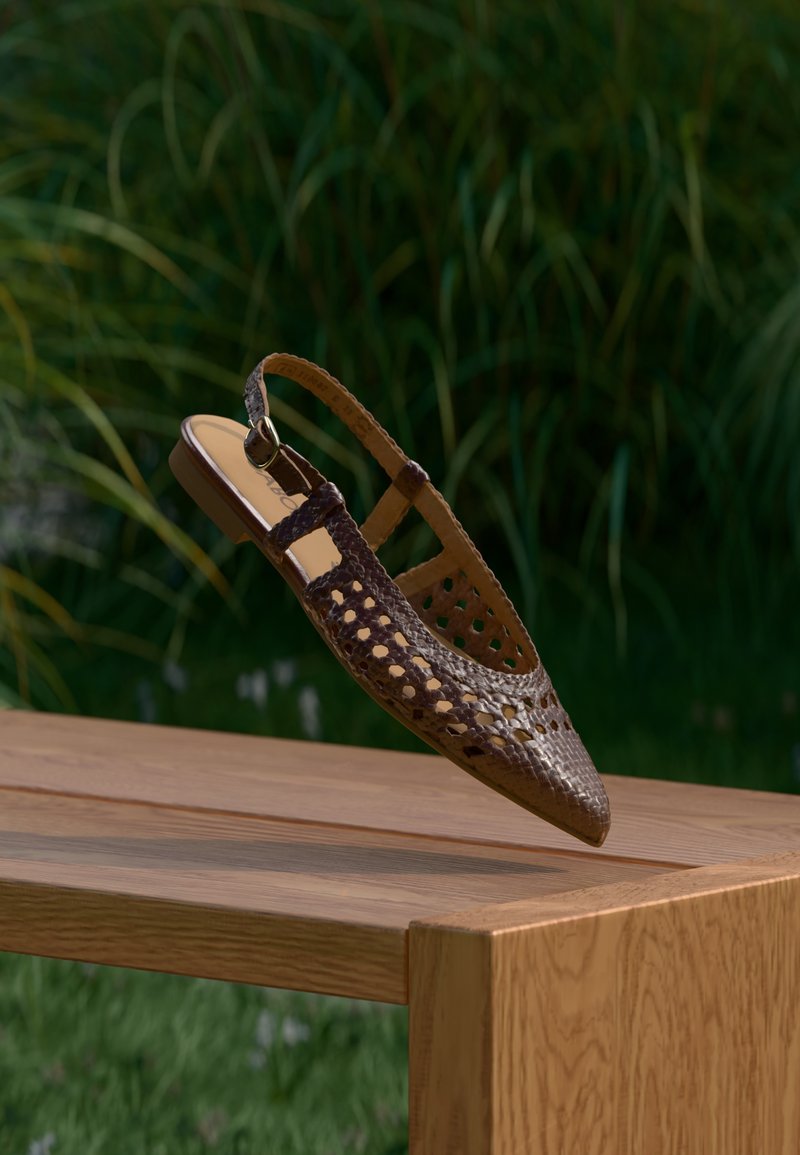 Καφέ πλεκτό παπούτσι με λουρί στο πίσω μέρος και μυτερή μύτη, που διαθέτει λεπτομέρειες με κοψίματα και επίπεδη σόλα, τοποθετημένο σε ξύλινη επιφάνεια.