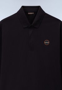 Crna polo majica od pamuka. Ima kratki ovratnik, placket sa tri dugmeta i tkanu oznaku na lijevoj strani prsnog koša.