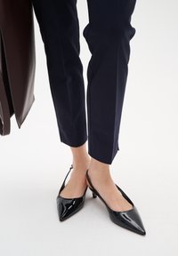 Svarta patentläderslingback-klackar med spetsig tå och en tunn medelhög klack, tillsammans med marinblå cropped byxor.