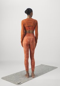 Athletic outfit with a rusty orange long-sleeve top and matching high-waisted leggings. Textured fabric, fitted design, and seamless details.