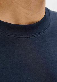 Mörkblå bomulls-T-shirt med rund halsringning, slät yta och plana sömmar, närbild på halsringningens detalj och övre bröstparti.