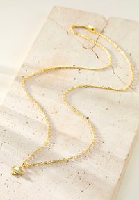 Gold necklace with a delicate chain and a small pendant featuring a clear gemstone, displayed on a textured stone surface.