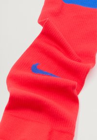 Élénk piros Nike zoknik, kék logóval. A szövet bordázott, szoros illeszkedésű és sima tapintású.