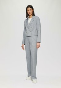 Grijze op maat gemaakte suit met een dubbelzijdige blazer en rechte broek, gemaakt van gestructureerde stof, gecombineerd met witte platform sneakers.