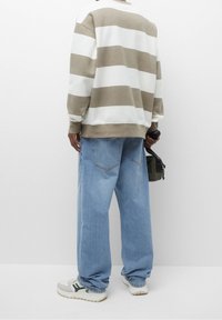 Sweatshirt oversize rayé marron clair et blanc, jeans bleu clair ample, et baskets grises avec des accents noirs ; tenant un petit sac vert.
