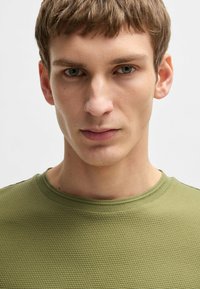 T-shirt verde oliva con texture, collo rotondo e maniche corte, caratterizzato da un motivo sottile e un design aderente.
