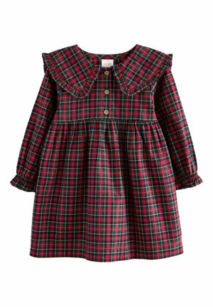 Enfant portant une robe à carreaux rouge et vert avec des boutons en bois et des volants près du col et de la taille.