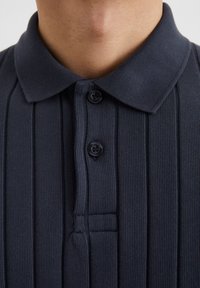 Navyblauwe polo met een gestructureerde brei, voorzien van een plat kraagje, twee zwarte knopen en een verticale ribbelstructuur aan de voorkant.