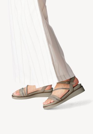 Gray sandal with multiple straps and buckle, featuring a textured sole and slight heel, paired with white, striped wide-leg pants.