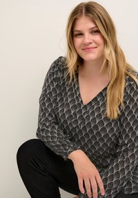 Černá blůza s výstřihem do V, s bílým abstraktním vzorem listů, měkká tkanina a nařasené rukávy, v kombinaci s černými kalhotami.