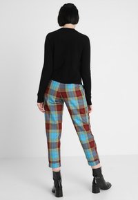 Pull noir, pantalon à carreaux bleu, rouge, gris et jaune, longueur cheville, porté avec des bottines noires à talons, vu de dos.