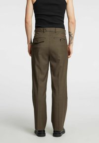 Brązowe spodnie z prostą nogawką, wykonane z teksturowanej tkaniny, z dwoma tylnymi kieszeniami i subtelnym wzorem. Połączone z czarnym topem na ramiączkach i butami.