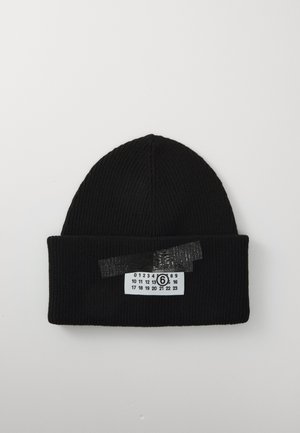 Bonnet en tricot côtelé noir avec un bord replié, portant une étiquette blanche imprimée avec des chiffres noirs et un numéro six entouré, fixé par du ruban noir.