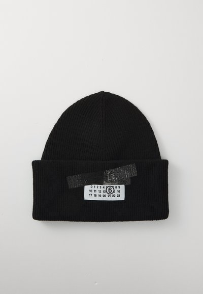 Czarna, prążkowana czapka beanie z zagiętym brzegiem, z białą metką z nadrukowanymi czarnymi cyframi oraz okrągłą cyfrą sześciu zabezpieczoną czarną taśmą.