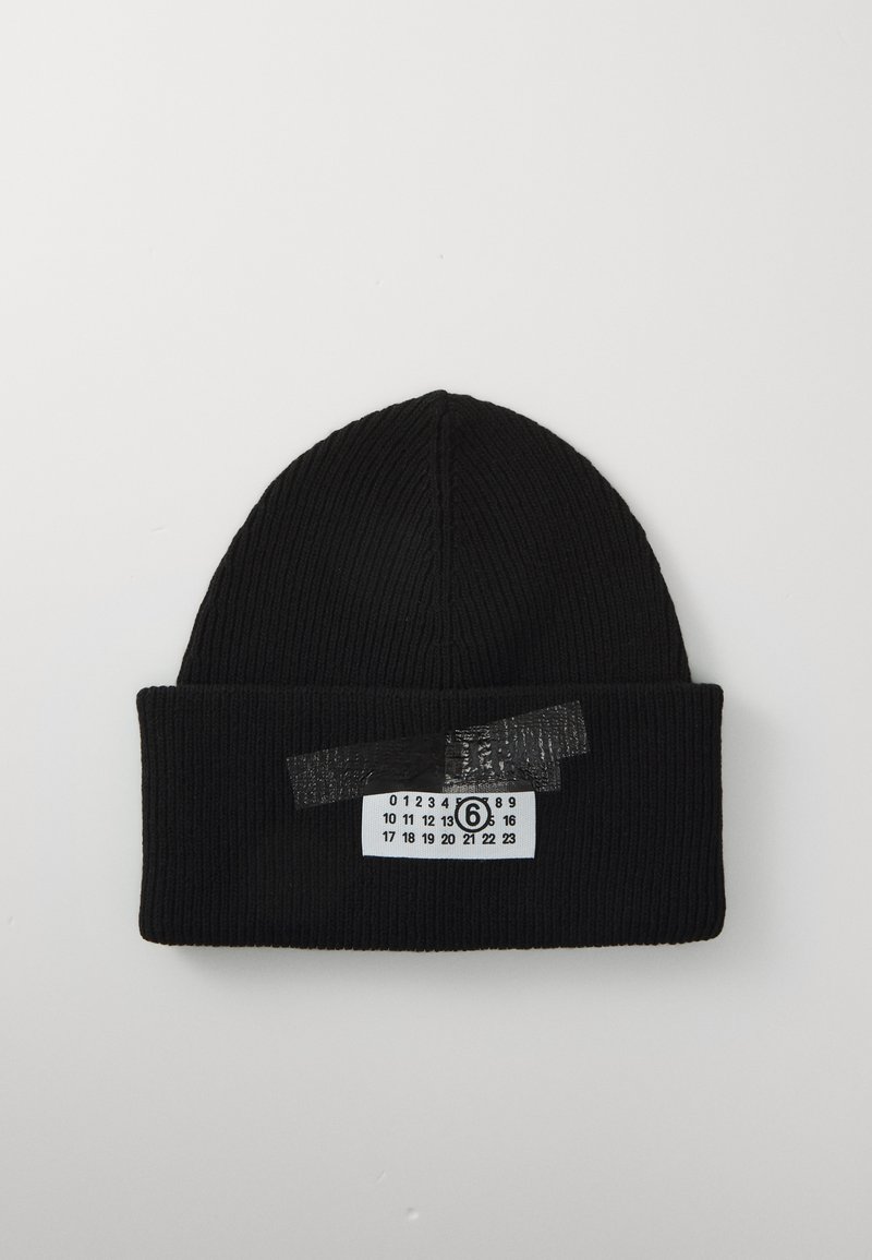 Melna ribbota adīta beanie cepure ar salocītu malu, kurai ir balta birka ar melniem cipariem un aplokotais cipars seši, pievienots ar melu lentes palīdzību.