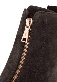 Bottine en daim gris foncé dotée d'une fermeture éclair latérale avec un tirette métallique rose doré et des coutures visibles le long des coutures.