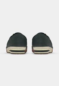 Μαύρα υφασμάτινα παπούτσια slip-on με μπεζ, μαύρη και καφέ σόλα, εμφανιζόμενα από πίσω σε λευκό φόντο.