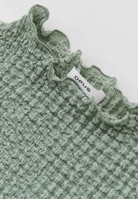 Textuur groene top met een smocked ontwerp, ruche neklijn en een wit label met "OPUS" aan de zijkant.