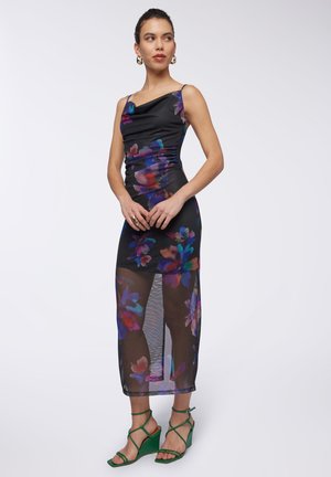 Abito nero con stampa floreale, corpetto arricciato e gonna trasparente. Sandali con tacco a spillo verdi completano il look. Design elegante con colori vivaci.