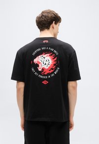 Μαύρο βαμβακερό t-shirt με κοντά μανίκια, διακοσμημένο με μεγάλο γραφικό μιας τίγρης που βρυχάται μέσα σε κόκκινε ς και λευκές φλόγες στην πλάτη.