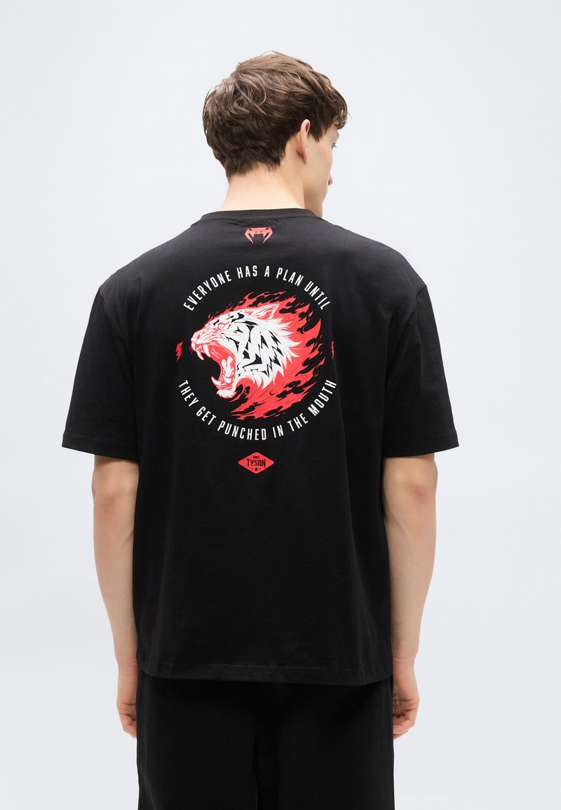 Μαύρο βαμβακερό t-shirt με κοντά μανίκια, διακοσμημένο με μεγάλο γραφικό μιας τίγρης που βρυχάται μέσα σε κόκκινες και λευκές φλόγες στην πλάτη.