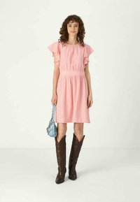 Vestido rosa até ao joelho com mangas franzidas, cintura elástica e um tecido texturizado. Combinado com botas de cowboy castanhas e uma bolsa azul clara.