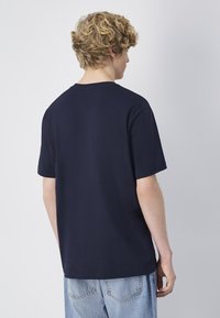 Camiseta de algodón navy con cuello redondo y mangas cortas, presenta un diseño liso y un corte relajado. Espalda mostrada sin texto ni gráficos.