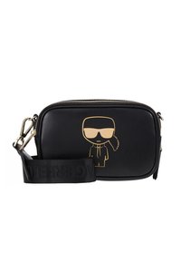Borsa a tracolla nera in pelle con grafica cartoon dorata, chiusura con zip e tracolla in tessuto con logo. Texture liscia, forma rettangolare.