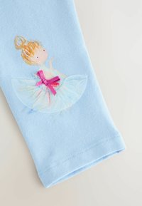 Hellblauer Stoff mit einer aufgedruckten Ballerina, goldenen Haaren im Dutt, weißem Tüllrock und einer pinken Schleife in der Taille.